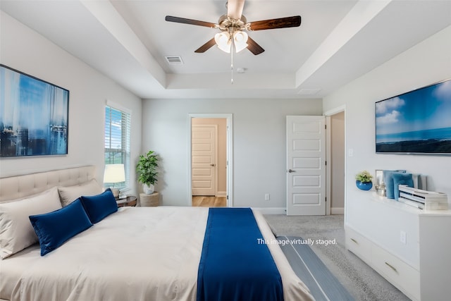 bedroom with ceiling fan, a raised ceiling, and light carpet