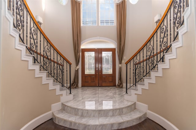 foyer entrance featuring light wood-type flooring, a towering ceiling, and french doors