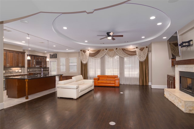 unfurnished living room featuring a tile fireplace, dark hardwood / wood-style floors, ceiling fan, and a raised ceiling