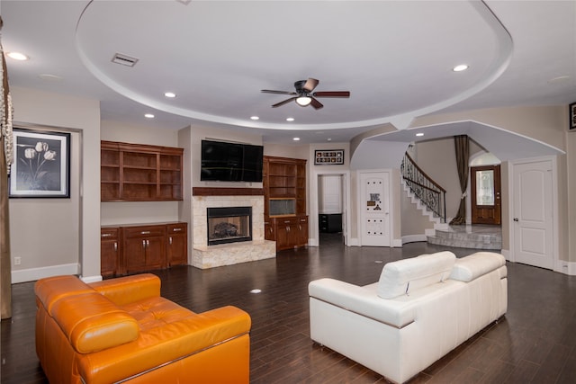 living room featuring ceiling fan, a fireplace, a raised ceiling, and dark wood-type flooring