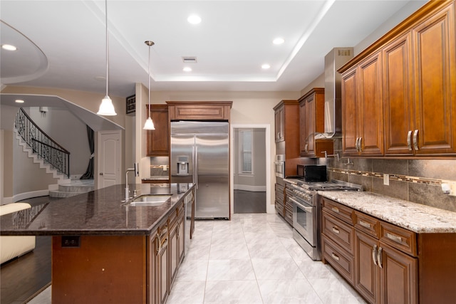 kitchen with high end appliances, pendant lighting, a tray ceiling, dark stone counters, and sink