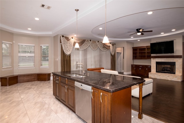 kitchen featuring hanging light fixtures, an island with sink, a fireplace, dark stone counters, and stainless steel dishwasher