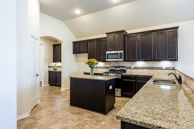 kitchen featuring light stone counters, lofted ceiling, sink, stainless steel appliances, and a center island