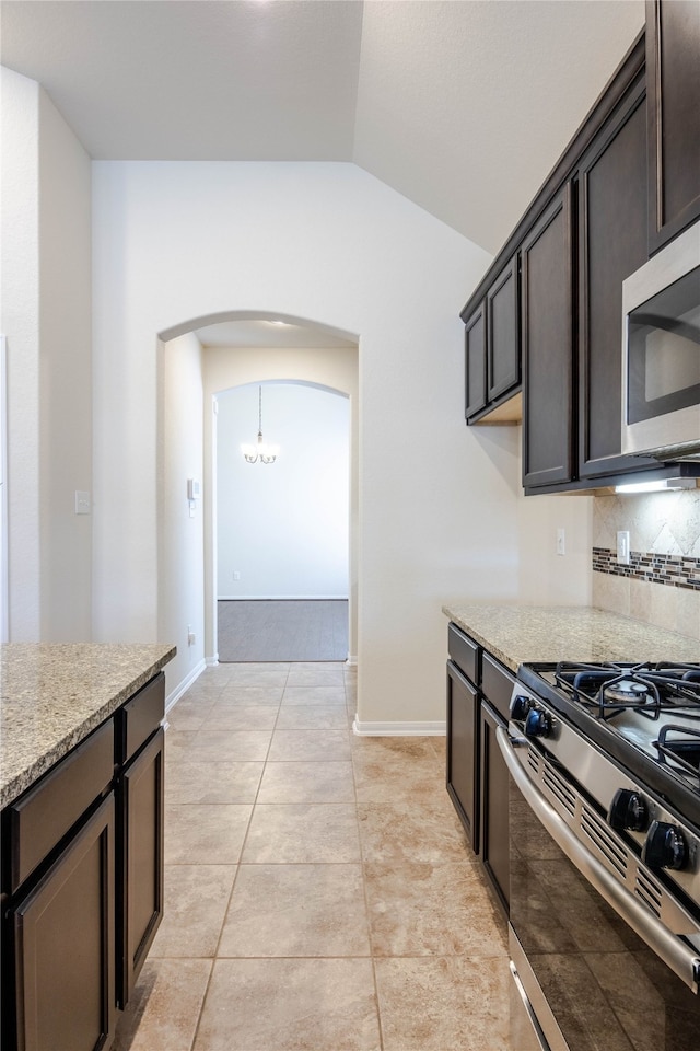 kitchen with light stone counters, light tile patterned floors, dark brown cabinets, stainless steel appliances, and vaulted ceiling