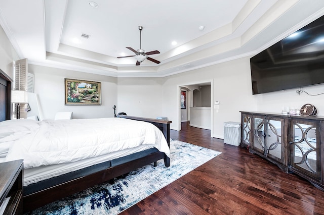 bedroom with ceiling fan, a raised ceiling, crown molding, and dark hardwood / wood-style flooring