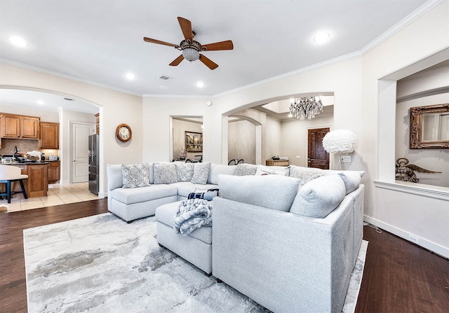 living room with ornamental molding, ceiling fan with notable chandelier, and light hardwood / wood-style floors