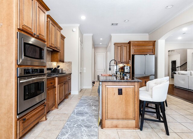 kitchen featuring ornamental molding, stainless steel appliances, a kitchen bar, and a kitchen island with sink