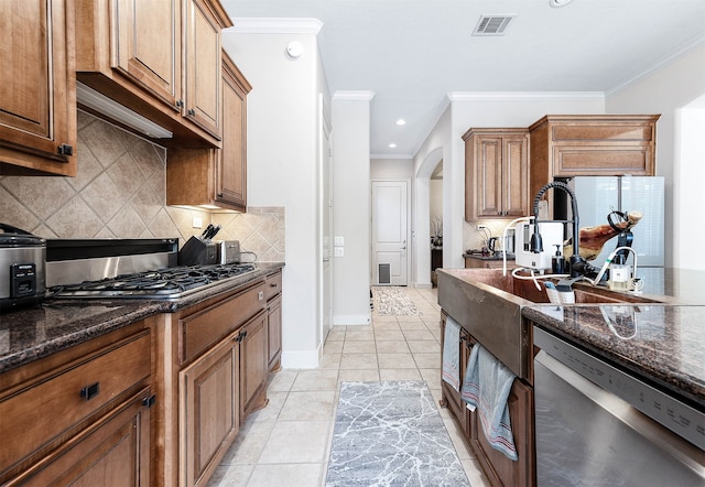 kitchen featuring ornamental molding, appliances with stainless steel finishes, light tile patterned floors, and dark stone counters