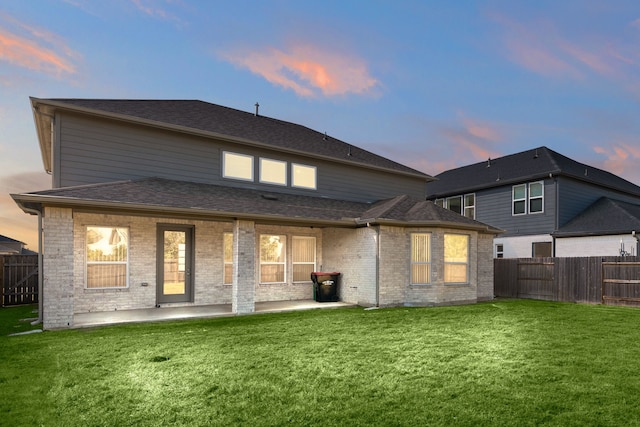 back house at dusk with a yard and a patio