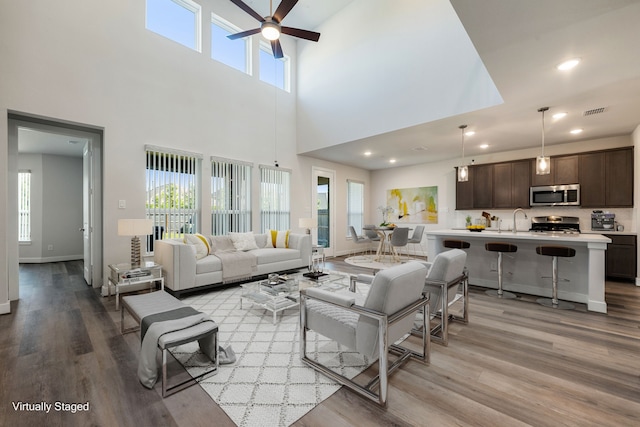 living room with a healthy amount of sunlight, a high ceiling, sink, and light hardwood / wood-style flooring