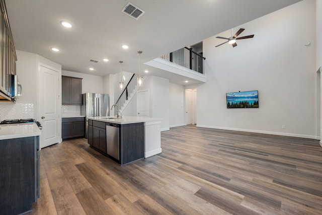 kitchen with backsplash, dark hardwood / wood-style flooring, decorative light fixtures, a center island with sink, and sink