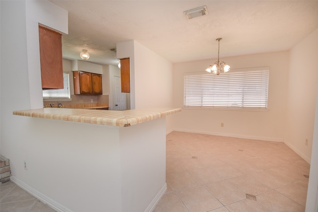 kitchen with kitchen peninsula, a breakfast bar area, light tile patterned floors, a chandelier, and pendant lighting