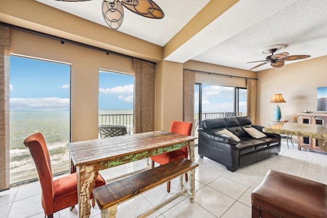 tiled dining room with ceiling fan, a textured ceiling, and a water view