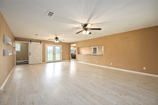 unfurnished living room with light hardwood / wood-style flooring, ceiling fan, and a barn door