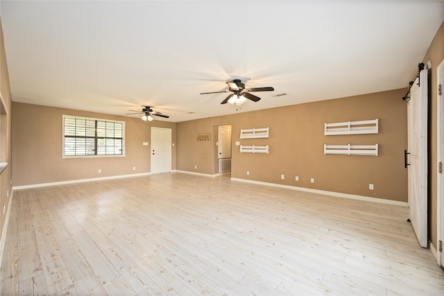 spare room featuring light hardwood / wood-style floors, ceiling fan, and a barn door