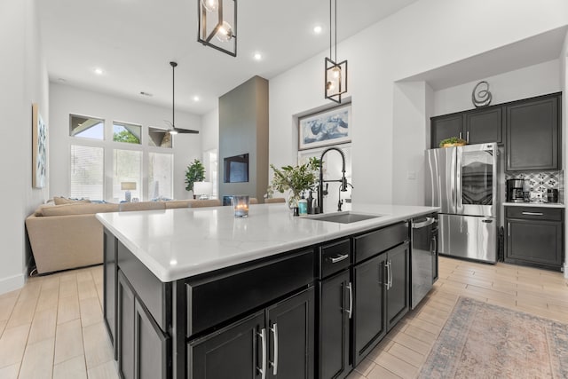 kitchen featuring tasteful backsplash, a kitchen island with sink, sink, hanging light fixtures, and appliances with stainless steel finishes