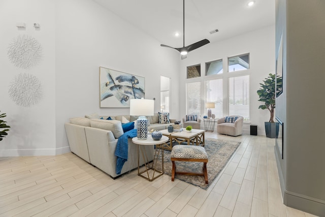 living room with light hardwood / wood-style flooring, a towering ceiling, and ceiling fan