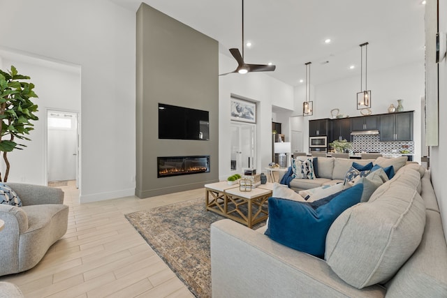 living room featuring ceiling fan, light wood-type flooring, and a towering ceiling