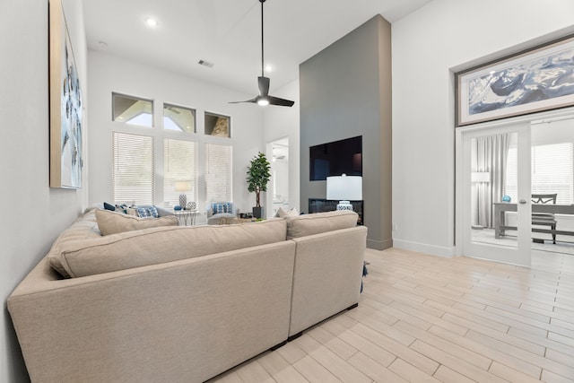 living room with light hardwood / wood-style flooring, a towering ceiling, and ceiling fan