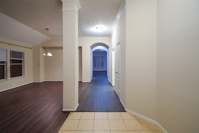 corridor featuring ornamental molding, light wood-type flooring, vaulted ceiling, and a textured ceiling