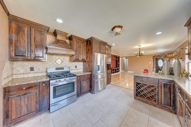 kitchen with light tile patterned flooring, appliances with stainless steel finishes, custom range hood, an inviting chandelier, and crown molding