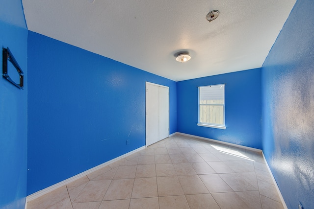 empty room with a textured ceiling and light tile patterned floors