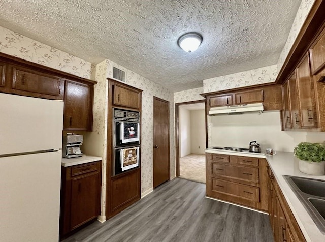 kitchen featuring a textured ceiling, white appliances, dark wood-type flooring, and sink