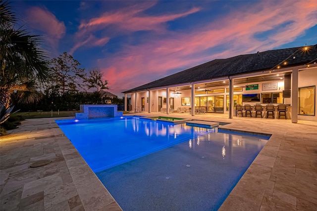 pool at dusk featuring a jacuzzi, a patio, and exterior bar