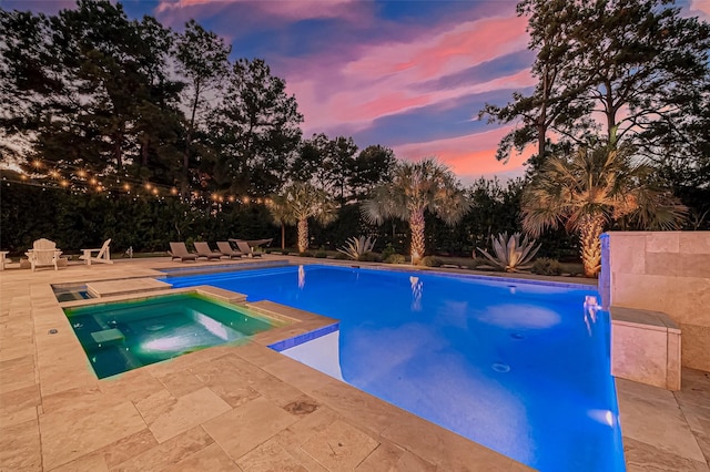 pool at dusk with an in ground hot tub and a patio