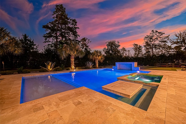 pool at dusk with an in ground hot tub and a patio