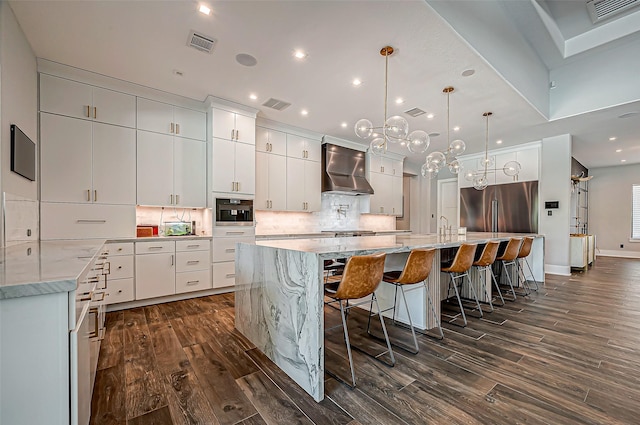 kitchen with pendant lighting, wall chimney range hood, a spacious island, white cabinets, and decorative backsplash