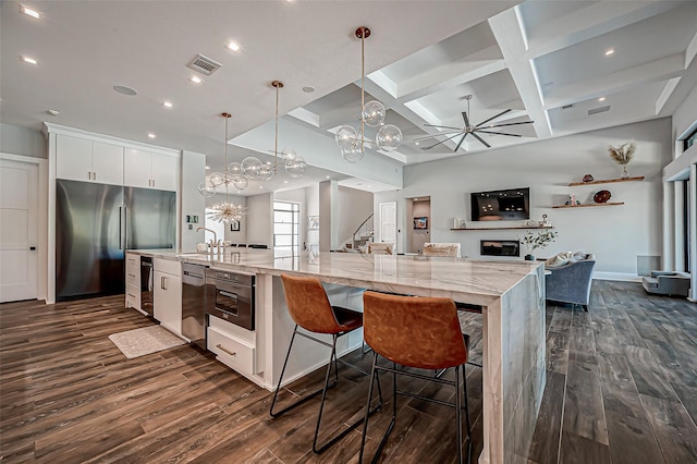 kitchen featuring pendant lighting, white cabinetry, stainless steel appliances, a spacious island, and light stone countertops