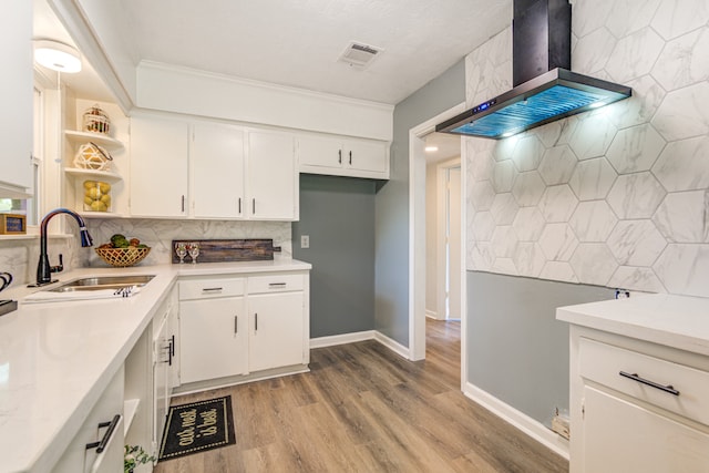 kitchen featuring light hardwood / wood-style floors, tasteful backsplash, sink, white cabinets, and wall chimney range hood