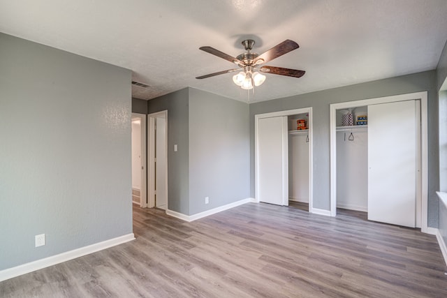 unfurnished bedroom featuring light hardwood / wood-style flooring, two closets, ceiling fan, and a textured ceiling