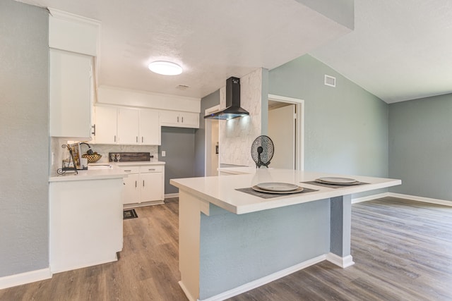 kitchen featuring decorative backsplash, white cabinetry, hardwood / wood-style flooring, and wall chimney range hood