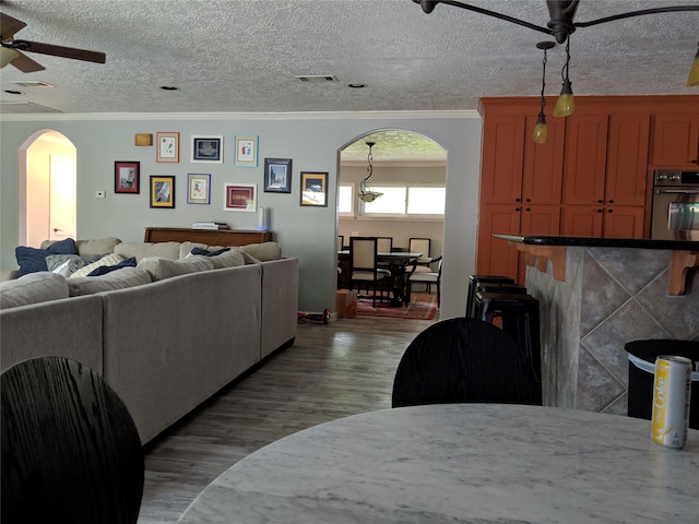 living room featuring ornamental molding, ceiling fan, hardwood / wood-style floors, and a textured ceiling