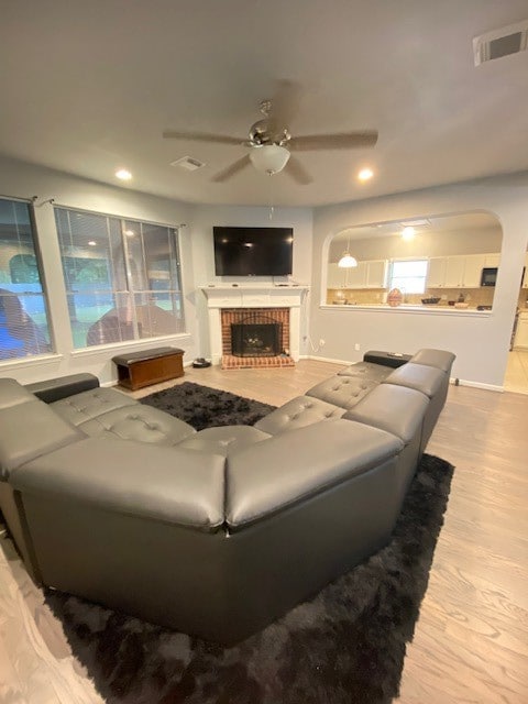 living room featuring a brick fireplace, light hardwood / wood-style floors, and ceiling fan