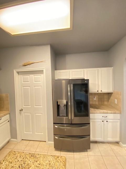 19603 Huckleberry Branch Ct, Spring, TX 77388 - kitchen with stainless steel refrigerator with ice dispenser, light tile patterned floors, tile countertops, white cabinets, and tasteful backsplash