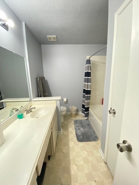 full bathroom with a textured ceiling, vanity, toilet, and shower / bath combination with curtain