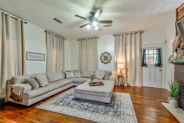 living room with ceiling fan, a textured ceiling, a fireplace, and dark hardwood / wood-style flooring