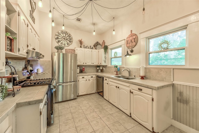 kitchen with white cabinetry, tasteful backsplash, stainless steel refrigerator, gas range, and tile counters