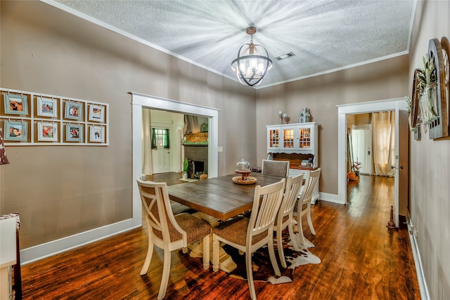 dining area featuring a textured ceiling, dark wood-type flooring, a notable chandelier, a fireplace, and ornamental molding