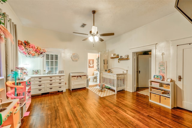 bedroom with ceiling fan, a nursery area, hardwood / wood-style floors, and a textured ceiling