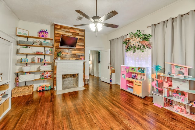 recreation room featuring crown molding, dark hardwood / wood-style floors, ceiling fan, and a brick fireplace