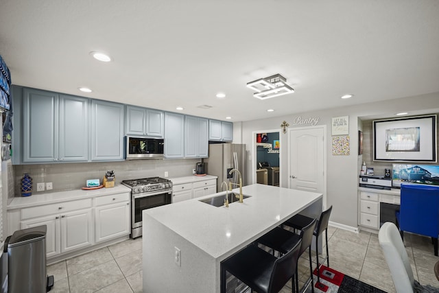 kitchen with tasteful backsplash, sink, an island with sink, appliances with stainless steel finishes, and washer and clothes dryer