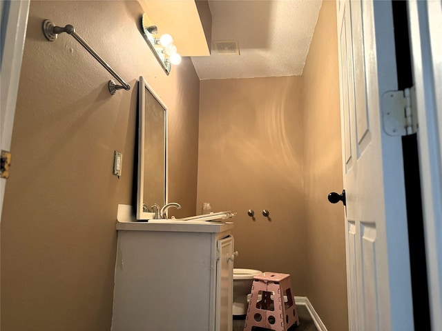 bathroom with toilet, vanity, visible vents, and baseboards