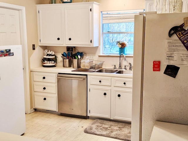 kitchen with light countertops, stainless steel dishwasher, freestanding refrigerator, white cabinets, and a sink