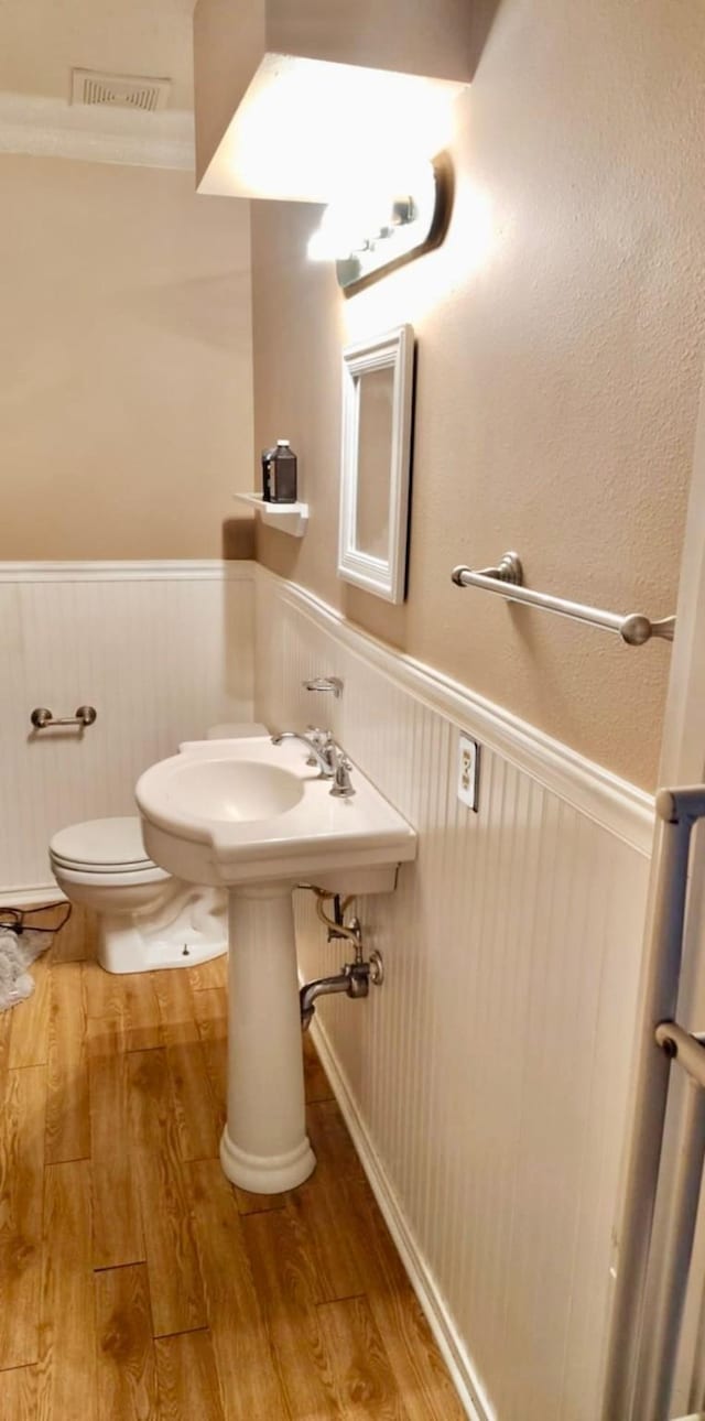 half bath featuring toilet, a wainscoted wall, visible vents, and wood finished floors