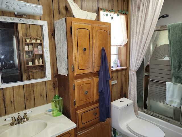 full bathroom with wooden walls, bath / shower combo with glass door, vanity, and toilet