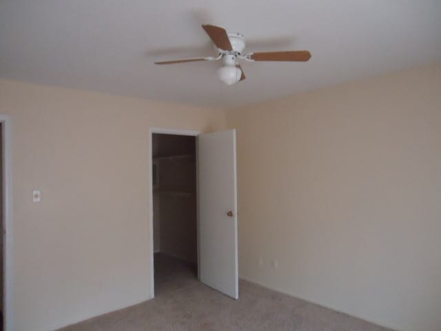 unfurnished bedroom with ceiling fan, light colored carpet, a closet, and a walk in closet